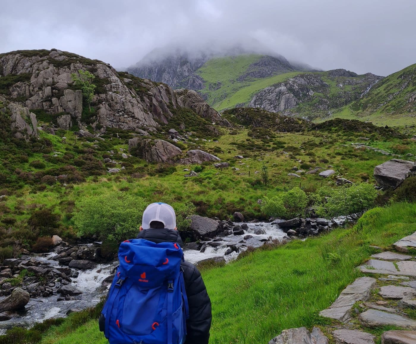 A young boy with his back to the camera, dressed in hiking gear and facing a misty mountain