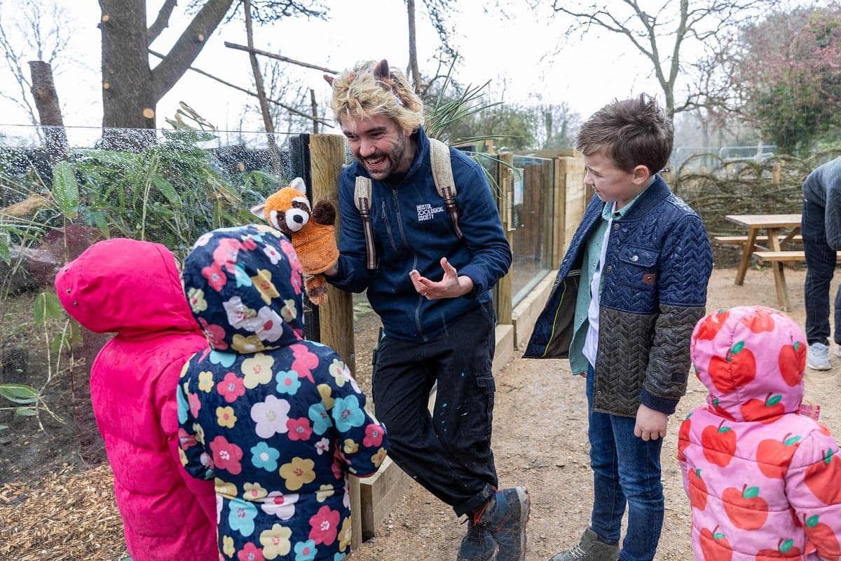 A member of zoo staff talking to a group of children and using a hand puppet