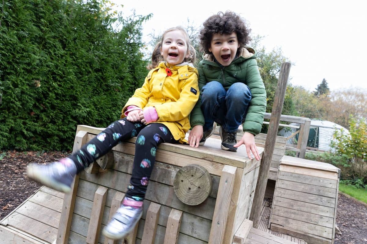 Two young children posing on top of a wooden tractor looking excited