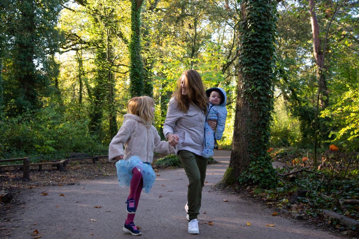 Mother holding a baby and her daughter's hand, skipping through the woods